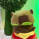 Capivara de pelúcia com roupa colorida e arranjo verde na decoração de festa infantil.