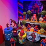 Cenário completo de festa infantil do Homem-Aranha com mesas decoradas, personagens e iluminação vermelha e azul.