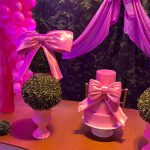 Arranjos ornamentais com laços rosa, gaiola decorativa e mesas de aniversário infantil.
