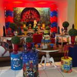 Vista lateral da decoração de aniversário dos Vingadores com personagens da Marvel, balões coloridos e mesas decoradas