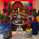 Decoração completa de aniversário dos Vingadores com cilindros personalizados, bolo temático e personagens em diferentes alturas.