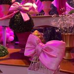 Gaiola branca decorativa com laço rosa de cetim e arranjos ornamentais em festa infantil.