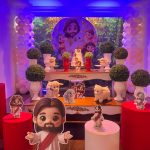 Cenário de aniversário infantil Jesus, o Bom Pastor, com painel ilustrado, balões em tons claros, mesas e personagens decorativos.