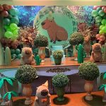 Mesa de festa infantil da capivara com bolo azul, cactos, pelúcias e decoração verde.